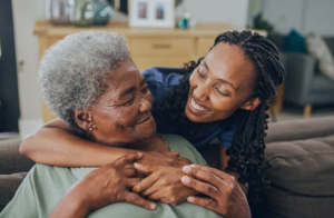 Caregiver embracing senior woman on couch, showing warmth and companionship, home care Elgin, IL