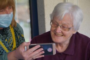 Caregiver showing smartphone to smiling elderly woman during home visit in Elgin IL